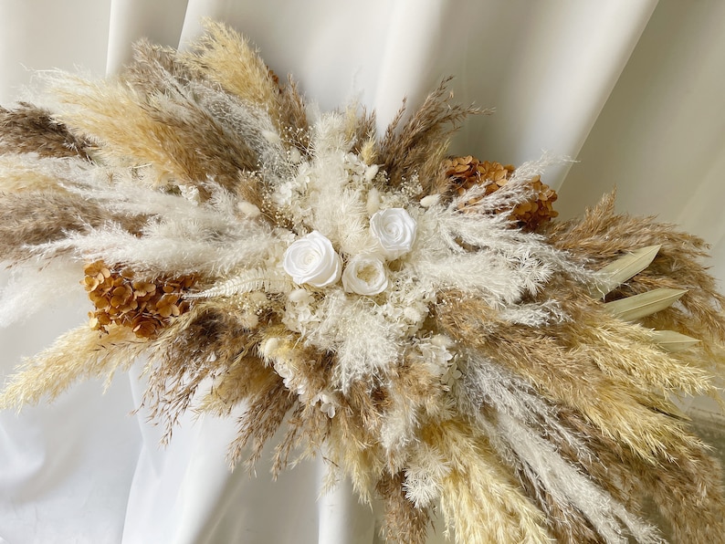 May include: A dried floral arrangement with white silk flowers and pampas grass in shades of beige and brown.
