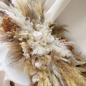 May include: A dried floral arrangement featuring white roses, pampas grass, and dried hydrangeas in shades of beige and brown.