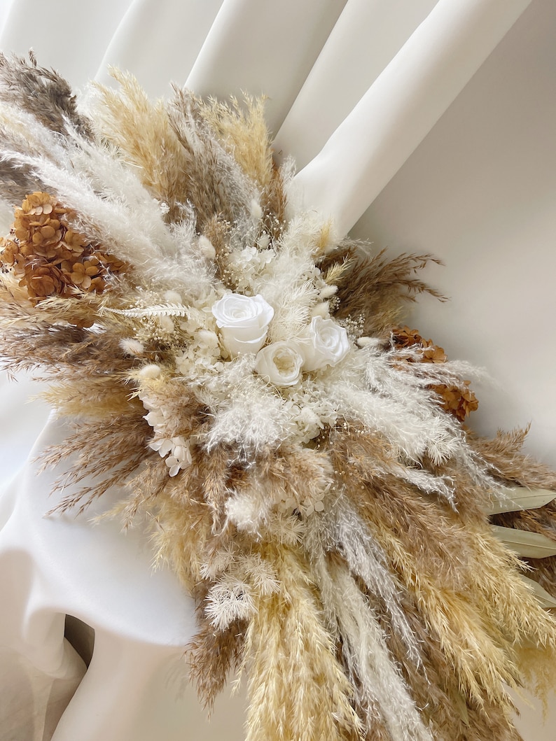 May include: A dried floral arrangement featuring white roses, pampas grass, and dried hydrangeas in shades of beige and brown.