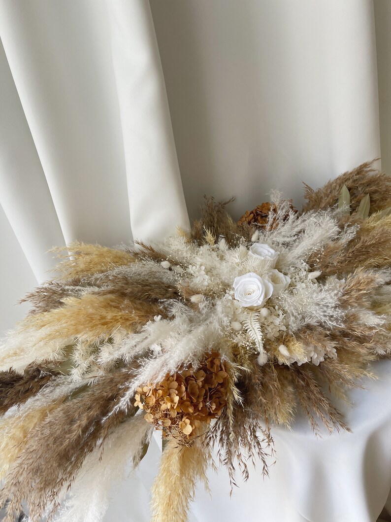May include: A dried floral arrangement with white and brown pampas grass, white roses, and brown hydrangeas.