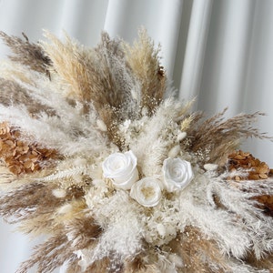 May include: A dried floral arrangement featuring white roses, white pampas grass, and brown pampas grass.