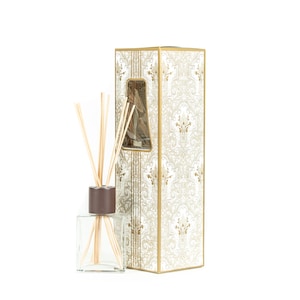 May include: A clear glass diffuser bottle with a brown cap and wooden reeds. The bottle is next to a decorative box with a gold and white patterned design.