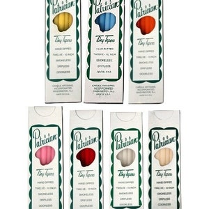 May include: A set of ten boxes of Patrician brand Tiny Tapers candles. Each box contains 12 candles, 10 inches long, and are hand-dipped, smokeless, dripless, and odorless. The boxes are arranged in two rows of five, with each row featuring a different color of candle: yellow, blue, orange, pink, red, white, and cream.