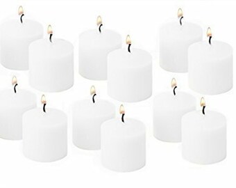 May include: A collection of twelve cylindrical white votive candles arranged in a grid. Each candle features a smooth wax exterior and a single lit wick with a small, visible flame. The candles are uniform in size and shape, standing upright.