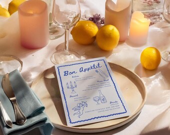 May include: A blue and white menu with the text "Bon Appetit" on a white tablecloth with candles, lemons, and glasses. The menu lists "Entrees", "Main Meal", "Dessert", and "Drinks".