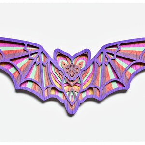 May include: A wooden bat cutout with a colourful striped pattern in shades of purple, pink, orange, yellow, and green. The bat is intricately designed with a layered effect, creating a 3D look.