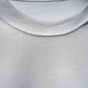 Peut inclure: Gros plan sur un sweat-shirt gris clair. Le col ras du cou c&ocirc;tel&eacute; est d'une nuance de gris l&eacute;g&egrave;rement plus fonc&eacute;e et est cousu sur le corps du v&ecirc;tement. Le tissu a une texture douce et l&eacute;g&egrave;rement floue.