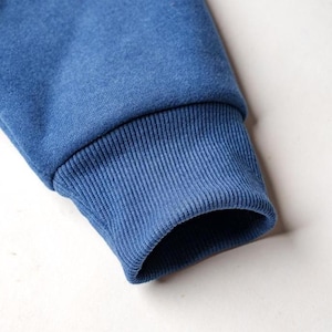 Peut inclure: Gros plan sur une manche de sweat-shirt bleu. Le poignet est c&ocirc;tel&eacute; et d'une nuance de bleu l&eacute;g&egrave;rement plus fonc&eacute;e que le reste de la manche. Le tissu semble doux et confortable.