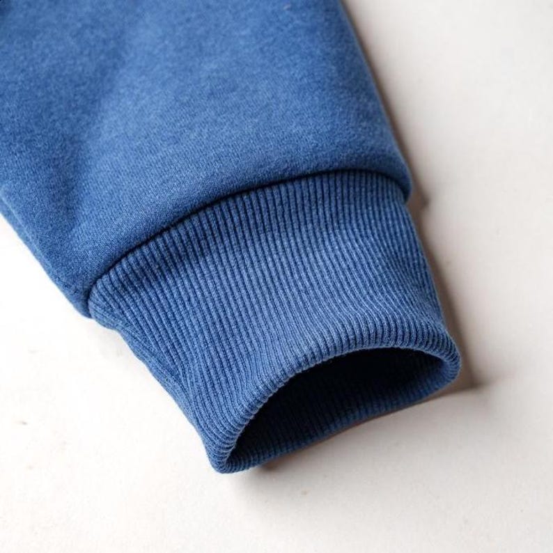 Peut inclure: Gros plan sur une manche de sweat-shirt bleu. Le poignet est c&ocirc;tel&eacute; et d'une nuance de bleu l&eacute;g&egrave;rement plus fonc&eacute;e que le reste de la manche. Le tissu semble doux et confortable.