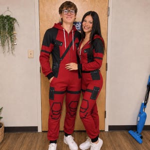 May include: Two matching red and black hooded jumpsuits featuring a front zip closure, long sleeves, and black utility-style pocket details on the legs and chest. The jumpsuits have a fitted design with white drawstrings at the hood.