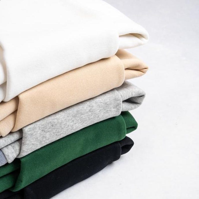Peut inclure: Une pile de sweatshirts pli&eacute;s de diff&eacute;rentes couleurs. Les couleurs comprennent le blanc, le beige, le gris, le vert et le noir. Les sweatshirts sont soigneusement empil&eacute;s, mettant en valeur les diff&eacute;rentes teintes et textures du tissu.
