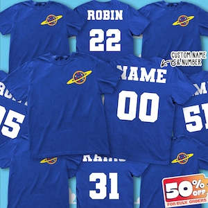 以下が含まれることがあります： 惑星のグラフィックと「CUSTOM NAME & NUMBER」の文字が入ったロイヤルブルーのTシャツ。 「ROBIN 22」、「NAME 00」、および「31」などの名前と番号が表示されているシャツもあります。 大量注文で50％オフのプロモーションが表示されています。
