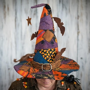 May include: A patchwork witch hat featuring a variety of Halloween-themed fabric patterns in orange, purple, black, and blue. The hat is adorned with brown felt bat cutouts, a wire-mounted star, and a brown textured band with a metal buckle.