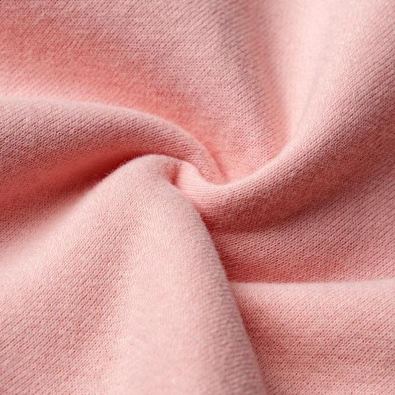 Peut inclure: Gros plan sur un tissu rose clair et doux avec un motif de tricot textur&eacute;. Le tissu est pli&eacute; et drap&eacute;, cr&eacute;ant des ombres et soulignant la texture. Le mat&eacute;riau semble &ecirc;tre un tricot, peut-&ecirc;tre du coton ou un m&eacute;lange similaire.