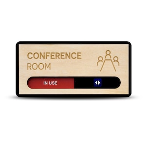 May include: A rectangular conference room sign with a light wood finish and a black border. The text "CONFERENCE ROOM" is engraved in dark letters next to a line-art icon of three people at a table. A sliding red indicator shows "IN USE".