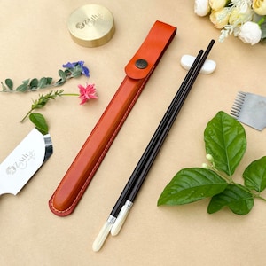 K&ouml;nnte beinhalten: Ein Set brauner Essst&auml;bchen mit wei&szlig;en Spitzen in einem braunen Lederetui. Die Essst&auml;bchen liegen auf einer wei&szlig;en Keramikablage. Das Etui hat einen Knopfverschluss und der Text "Zmith Craft" ist auf das Etui gepr&auml;gt.