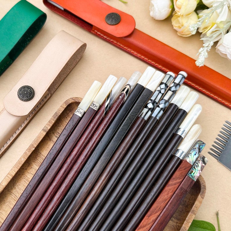K&ouml;nnte beinhalten: Ein Set mit 14 Paar Essst&auml;bchen mit verschiedenen Designs aus Holz und Perlmutt. Die Essst&auml;bchen sind in einem Holztablett angeordnet und bereit f&uuml;r eine Mahlzeit.