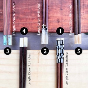 Puede incluir: Cinco pares de palillos con puntas de diferentes colores y longitudes. Los palillos est&aacute;n hechos de madera oscura y tienen un acabado natural. Las puntas est&aacute;n hechas de n&aacute;car blanco y negro. Los palillos est&aacute;n dispuestos en una fila sobre una superficie de madera. Las longitudes de los palillos son 25 cm, 24 cm, 23 cm, 25 cm y 25 cm.