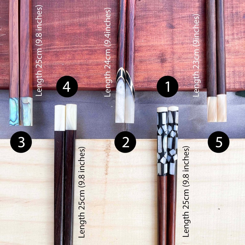 Puede incluir: Cinco pares de palillos con puntas de diferentes colores y longitudes. Los palillos est&aacute;n hechos de madera oscura y tienen un acabado natural. Las puntas est&aacute;n hechas de n&aacute;car blanco y negro. Los palillos est&aacute;n dispuestos en una fila sobre una superficie de madera. Las longitudes de los palillos son 25 cm, 24 cm, 23 cm, 25 cm y 25 cm.