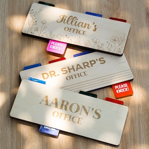 May include: Three rectangular light-colored wooden office signs with engraved text. The top sign reads Jillian's OFFICE with floral line art. The middle sign reads DR. SHARP'S OFFICE. The bottom sign reads AARON'S OFFICE. Each sign has colorful sliding tabs.