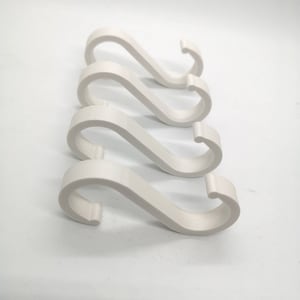 Op de afbeelding: Vier witte S-vormige haken van plastic. De haken zijn in een rij geplaatst, met de bovenste haak iets verschoven.
