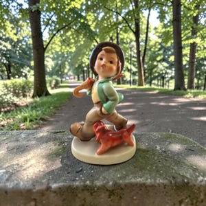 May include: A ceramic figurine of a young boy in a green jacket and brown pants, walking with a red dog. The boy wears a brown hat and carries a stick over his shoulder. The figurine is on a beige base.