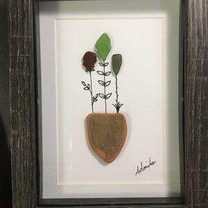 May include: A framed artwork featuring a hand-crafted floral arrangement made from sea glass and painted on a white background. The artwork is signed "Adoniika" in the bottom right corner.