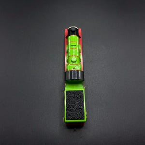 Könnte beinhalten: Ein grüner und schwarzer Spielzeug-Zugmotor mit roter Basis. Der Motor hat einen schwarzen Schornstein und ein schwarzes Gesicht mit einem weißen Kreis für ein Auge.