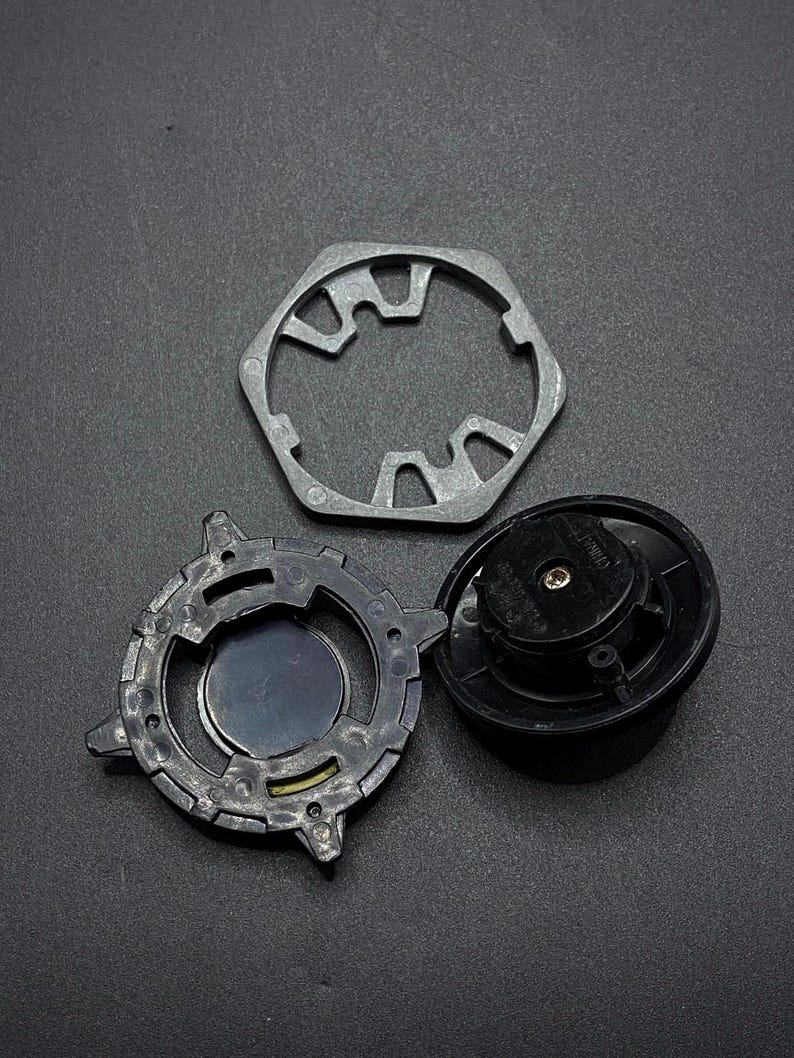 K&ouml;nnte beinhalten: Drei Metallteile f&uuml;r ein Beyblade-Spielzeug. Die Teile sind ein silberner sechseckiger Rahmen, ein schwarzer Kreisel mit silberner Mitte und ein silbernes sternf&ouml;rmiges Teil mit schwarzer Mitte.