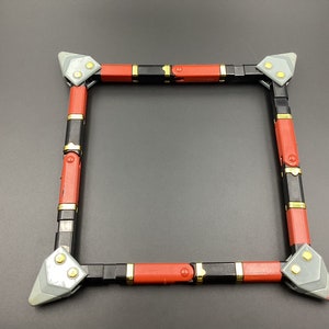 May include: A square frame made of black and red plastic with gold accents. The frame is made of multiple pieces that connect together.