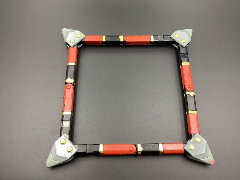 May include: A square frame made of black and red plastic with gold accents. The frame is made of multiple pieces that connect together.