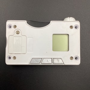 Może przedstawiać: Białe, ręczne urządzenie elektroniczne z zielonym ekranem, trzema przyciskami i małym czarnym suwakiem. Urządzenie ma nadrukowany tekst "S00310" na boku.