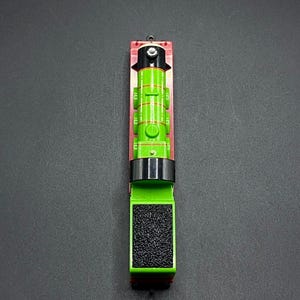 Puede incluir: Un tren de juguete verde y rojo con una chimenea negra y una cara negra. El motor tiene un vagón de carbón negro en la parte superior.