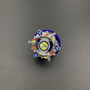 May include: A blue and silver Beyblade with a yellow and red design. The Beyblade has a star-shaped design with a central core and a spinning ring.