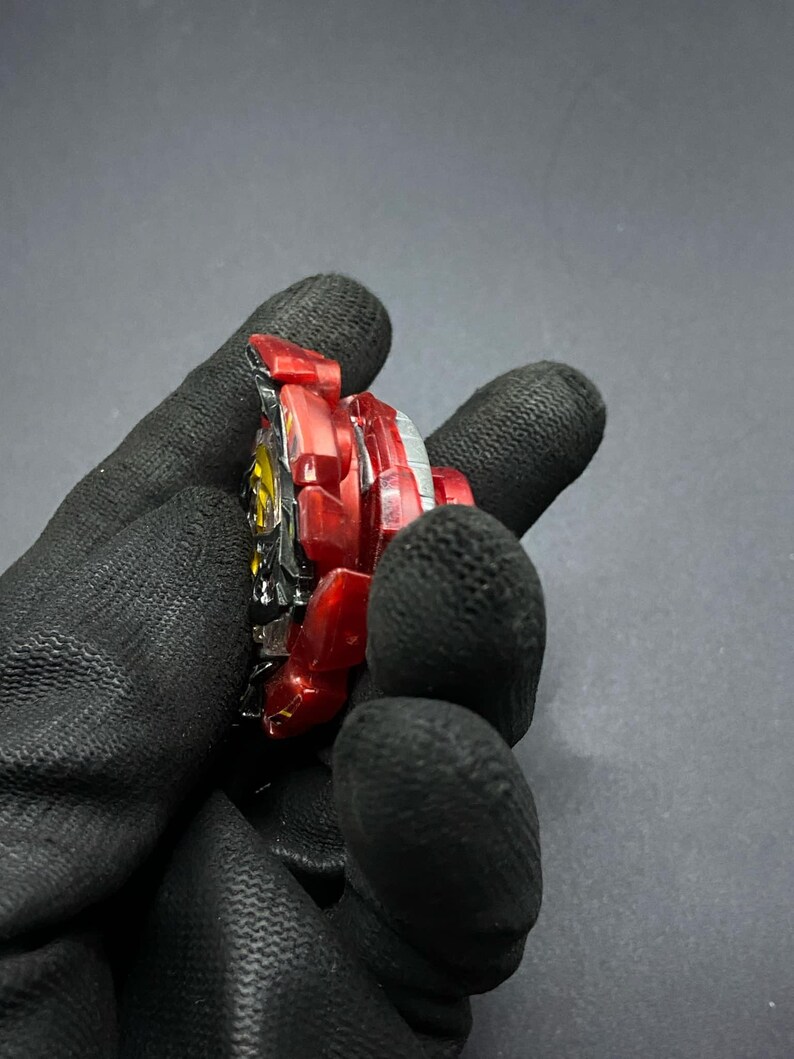 K&ouml;nnte beinhalten: Ein rotes und schwarzes Kreiselspielzeug mit einer durchsichtigen Plastikscheibe und einer Metallbasis.