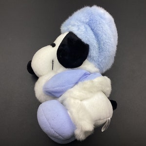May include: A white plush toy dog wearing a blue hat and scarf. The dog is sitting with its head tilted to the side.