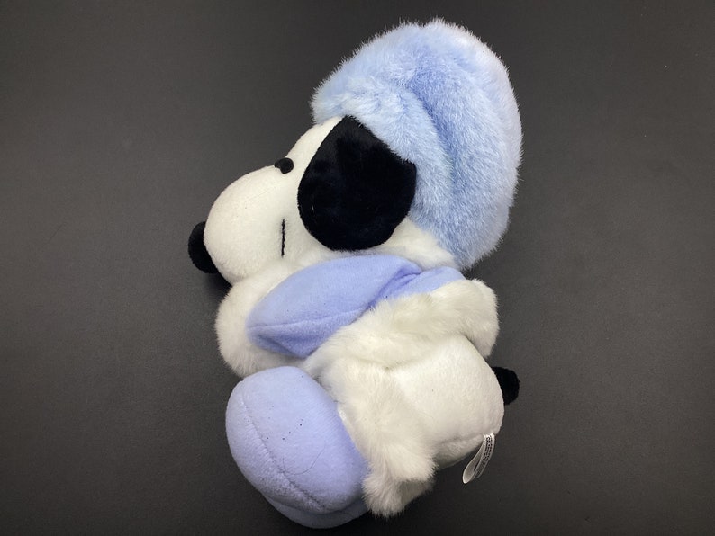 May include: A white plush toy dog wearing a blue hat and scarf. The dog is sitting with its head tilted to the side.