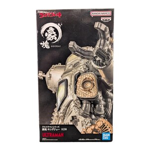 May include: A rectangular product box featuring a silver and metallic gold robot figure. The packaging displays the text Ultraman, Goukai, and Bandai Namco. The box art shows a detailed mechanical character with a claw-like arm, textured panels, and dark grey accents against a black background.