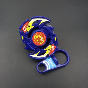 May include: A blue and yellow spinning top toy with a red and yellow center design. The toy has a handle and a ring for launching. The text "Draciel G" is visible on the side. A classic toy for children.