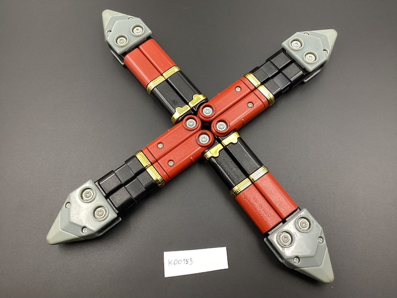 May include: Four black and red folding knives with gray handles and silver accents. The knives are arranged in a cross shape.