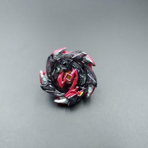 May include: A black and red spinning top with a silver center. The top has a sharp, angular design with a pointed tip.