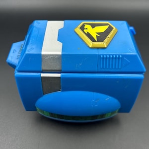 Puede incluir: Una taza de cerámica blanca con un asa negra y el texto "But First, Coffee" en negrita negra. La taza se encuentra sobre un fondo borroso, resaltando su diseño limpio.