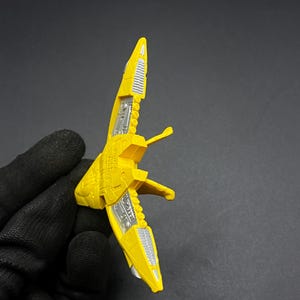 May include: A yellow plastic toy spaceship with silver details. The spaceship has a pointed nose and two wings.
