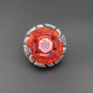 Könnte beinhalten: Ein kreisförmiges Kreiselspielzeug mit einem transparenten orangefarbenen Kunststoffkern, auf dem oben das Wort HYBRID und unten WHEEL aufgedruckt ist. Die Mitte enthält eine rote sechseckige Schraube mit weißer Grafik und blauen Akzenten.
