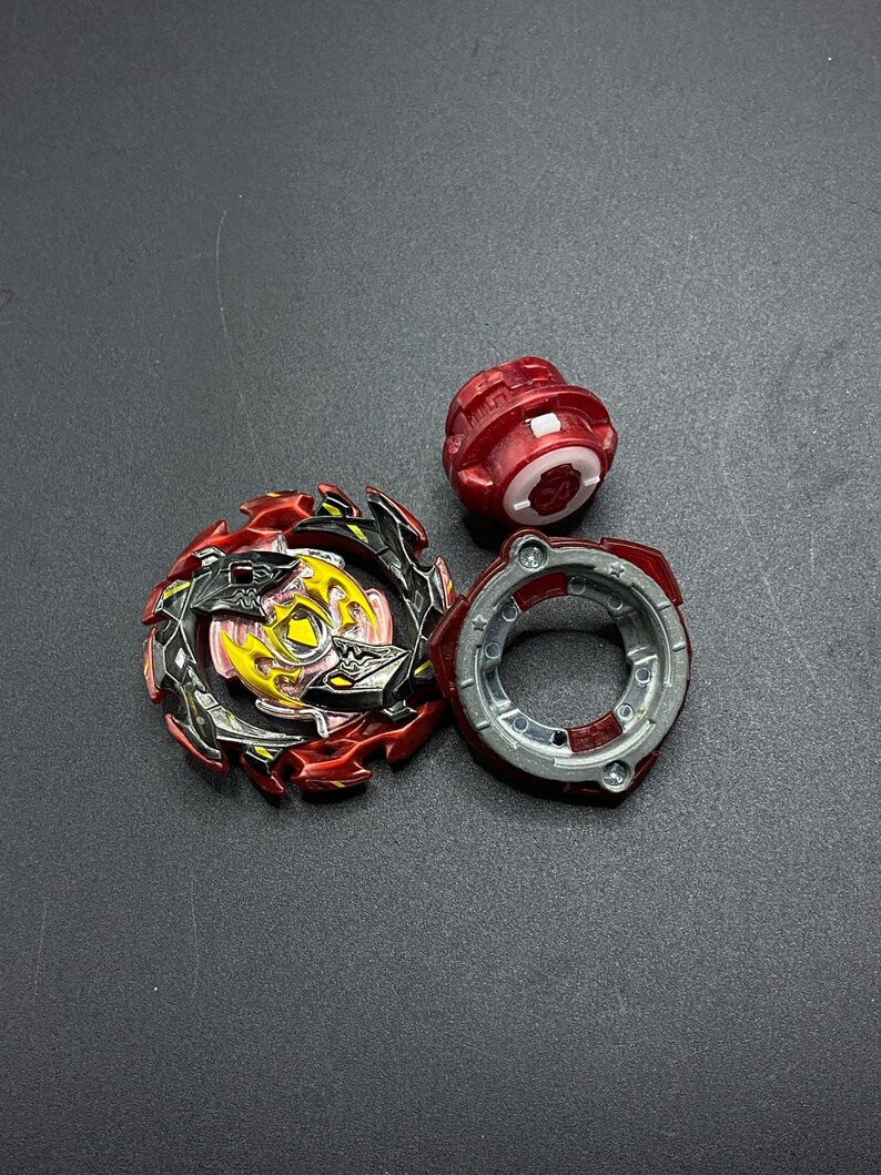 K&ouml;nnte beinhalten: Ein rotes, schwarzes und gelbes Beyblade mit einer silbernen und roten Performance-Spitze und einem roten Launch-Gear.