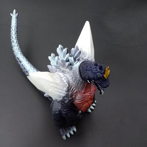 Peut inclure: Figurine détaillée d'un monstre ressemblant à Godzilla. La figurine présente une tête bleu foncé, une poitrine rouge et un corps blanc et bleu. La figurine a une longue queue et un dos épineux.