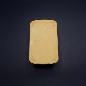 May include: A rectangular, light yellow box with rounded corners. The box has a slightly textured surface and delicate floral designs in each corner. The background is a solid, dark blue.