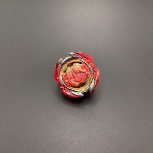 May include: A red and black spinning top toy with a gold centre. The top has a unique design with sharp edges and a circular centre.