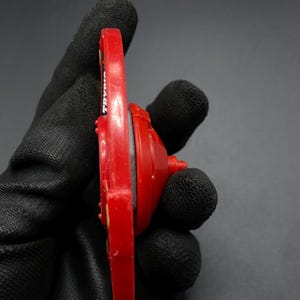 May include: Red and black plastic toy top with the word "TRAVLER" printed on the side.