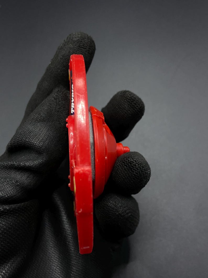 May include: Red and black plastic toy top with the word "TRAVLER" printed on the side.